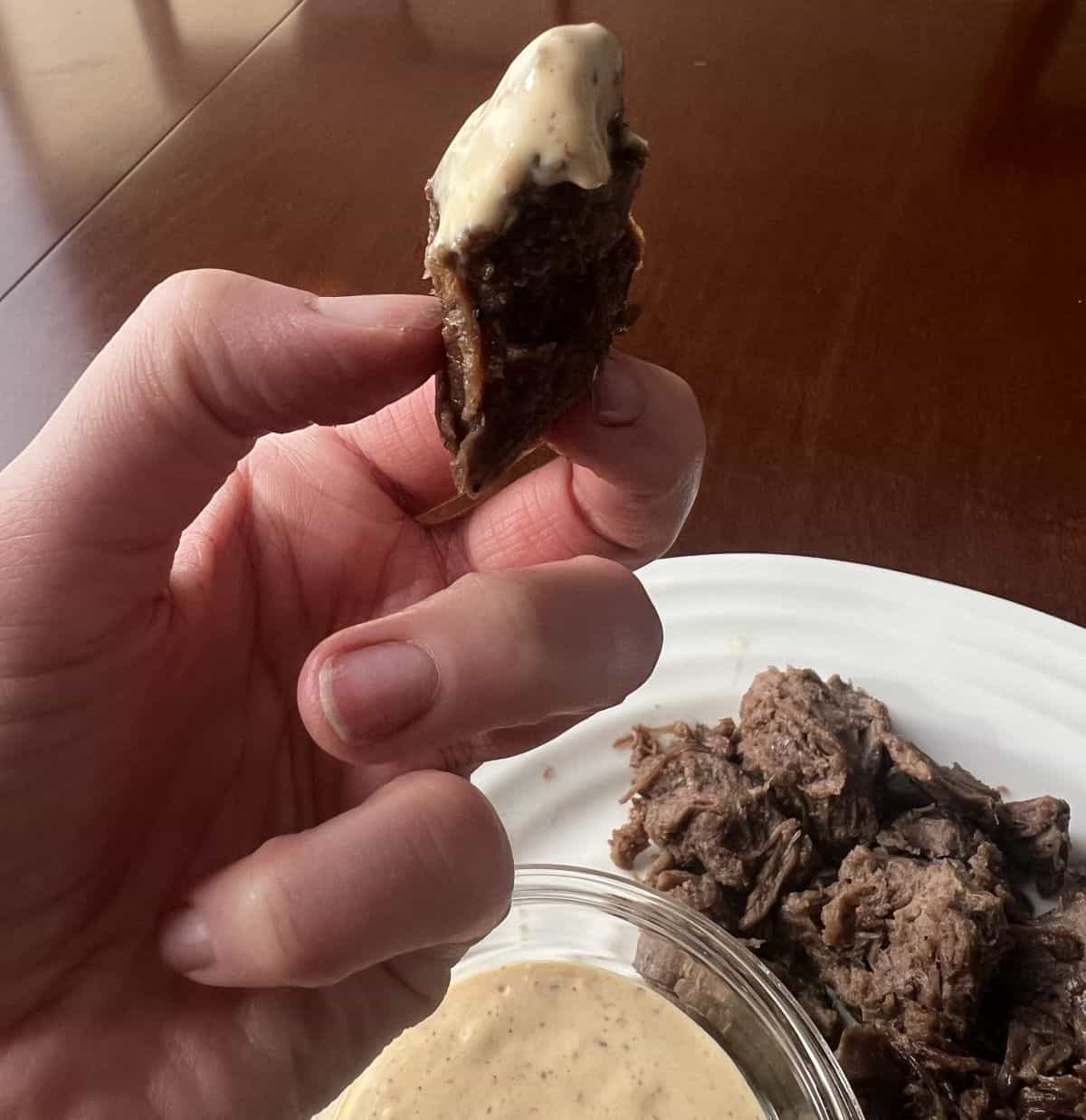 Image of a hand holding a steak bite dipped in sauce. 