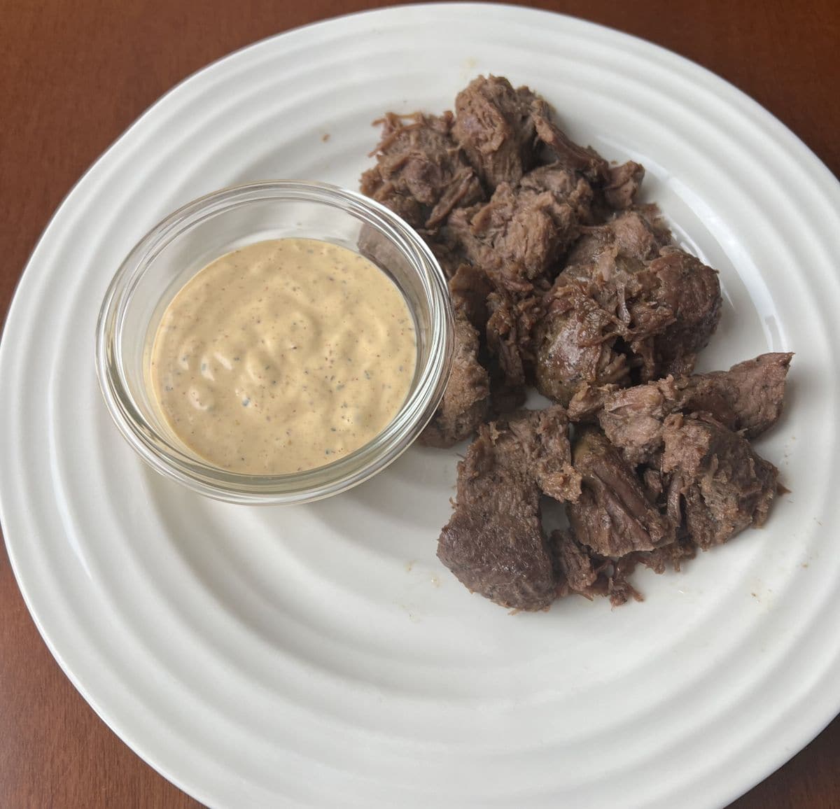 Image of the steak bites heated up and served on a white plate beside a bowl of sauce. 