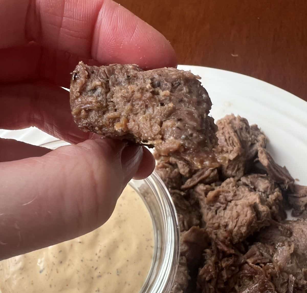 Closeup image of a hand holding a steak bite over a plate of steak bites.