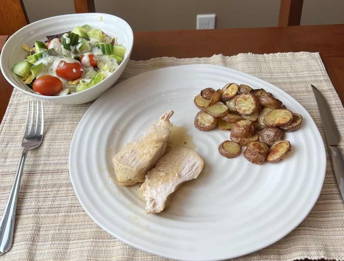 Image of cooked turkey breast served on a white plate beside potatoes and a side salad.