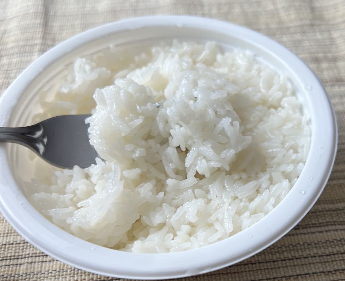Image of a forkful of rice hovering over a container of cooked rice.