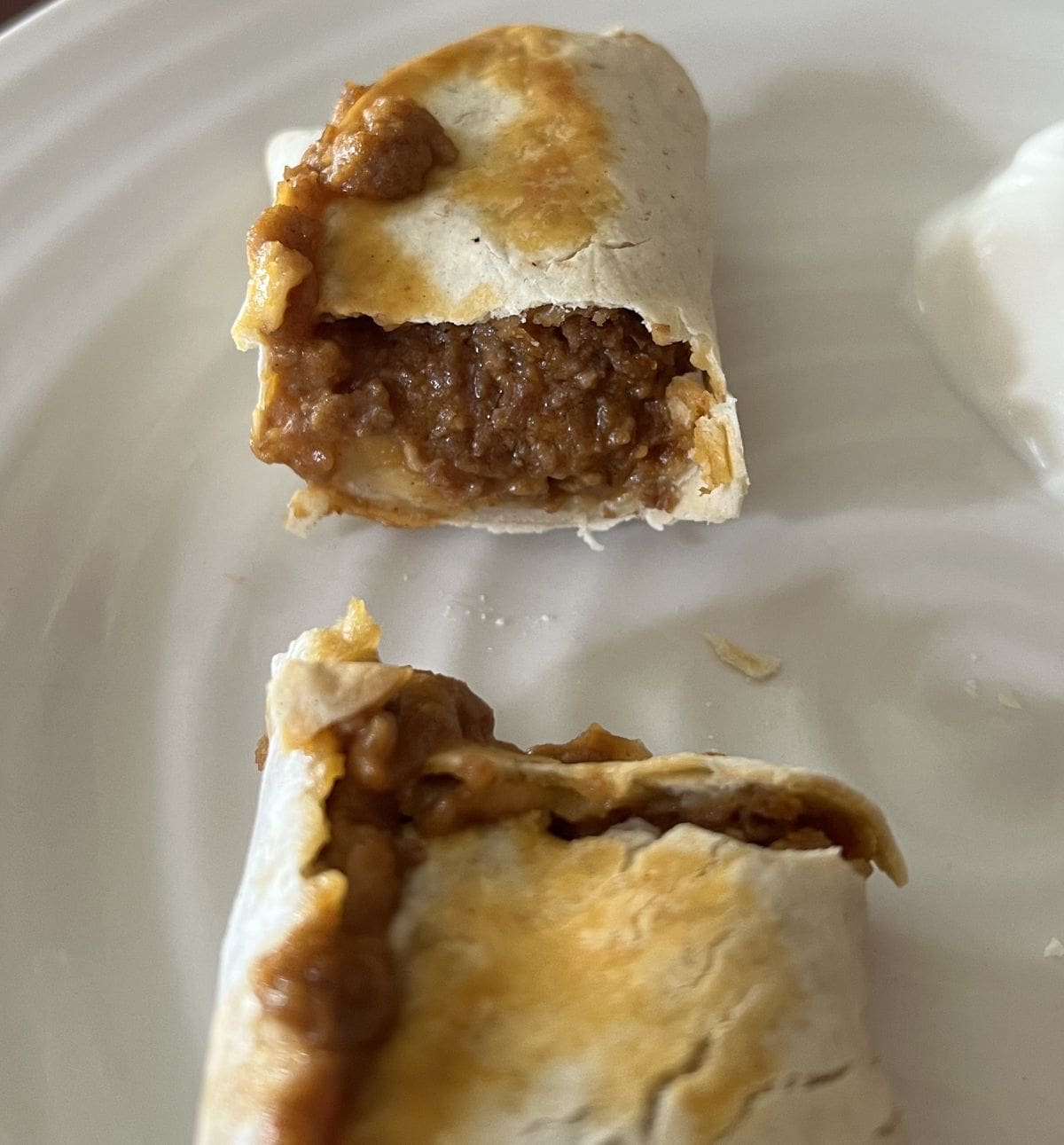 Closeup image of one cooked burrito served on a white plate and cut in half so you can see the filling inside. 