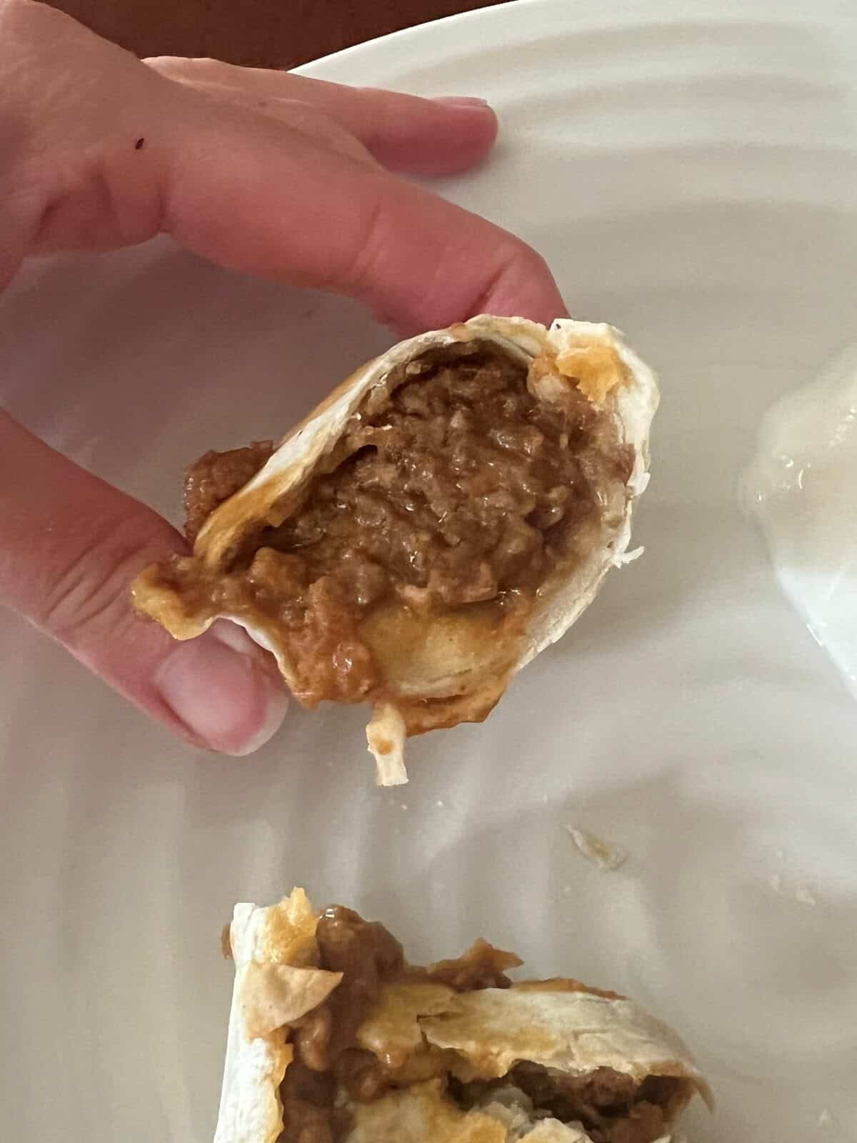 Image of a hand holding a burrito that's been cut in half close to the camera so you can see the filling inside.