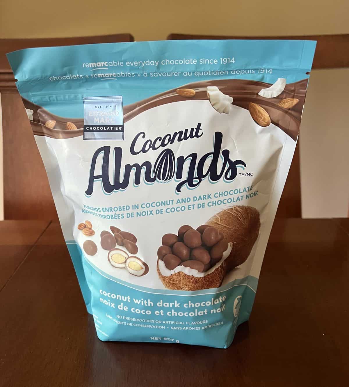 Image of the Costco Edward Marc Chocolatier Coconut Almonds bag sitting on a table unopened. 
