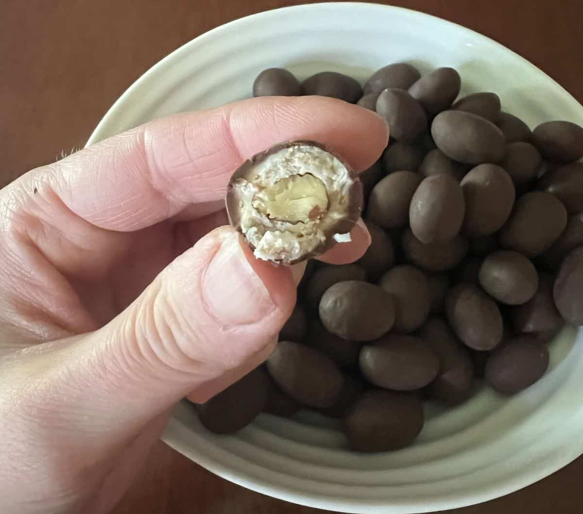 Image of a hand holding one coconut almond with a bite taken out of it so you can see the almond in the center and coconut filling.