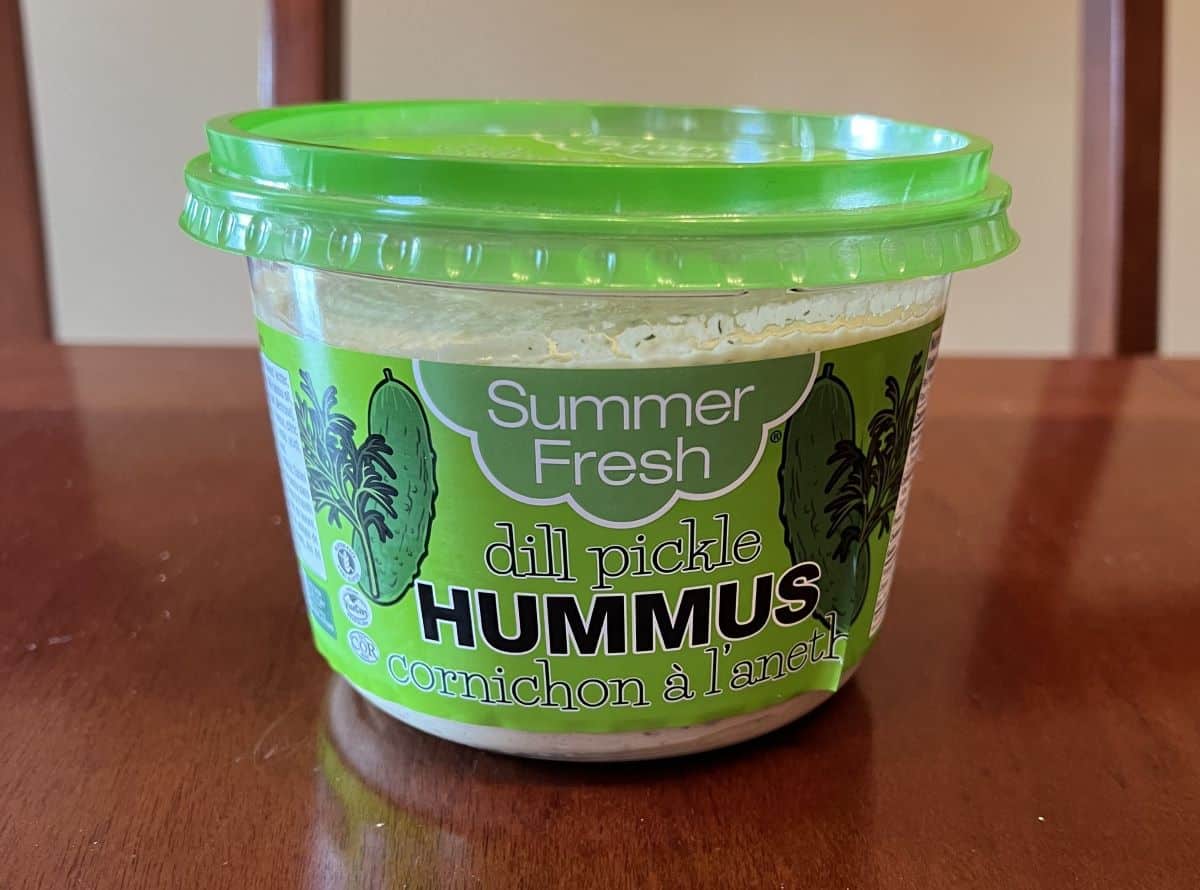 Image of the Costco Summer Fresh Dill Pickle Hummus container unopened sitting on a table. 