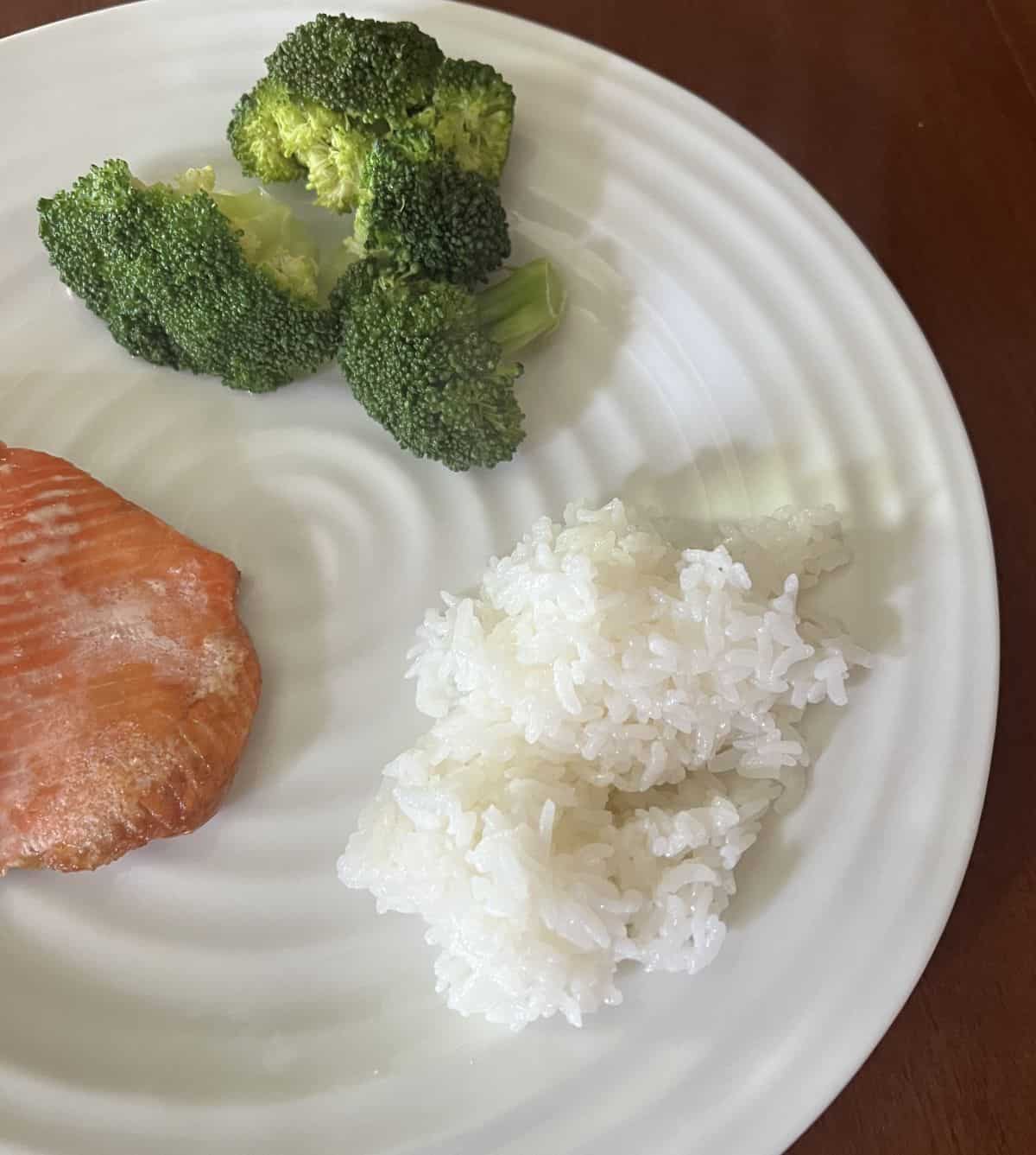 Closeup image of the sticky rice served on a white plate beside salmon and broccoli. 
