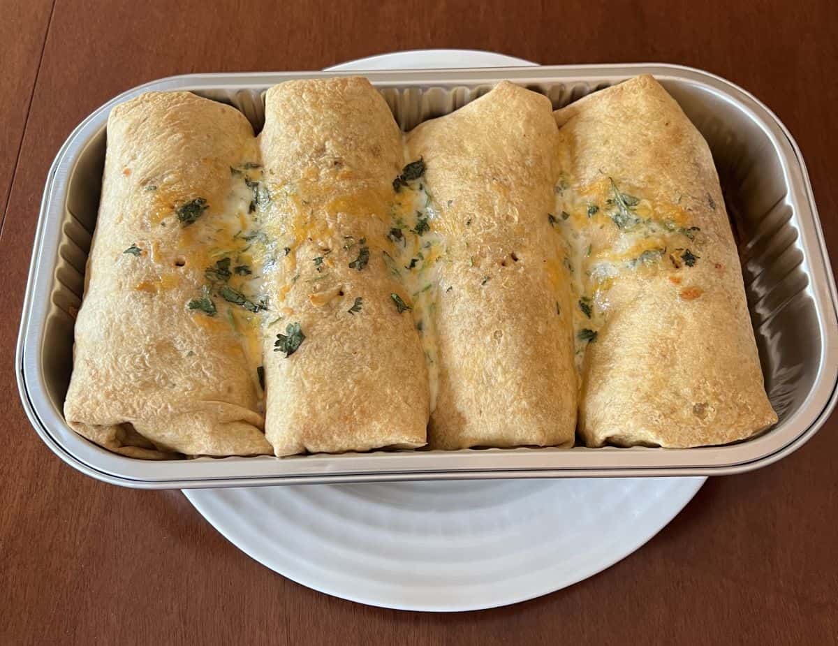 Image of four pork carnitas burritos in cooked in the tray they come and served on a table. The cheese is melted on top. 