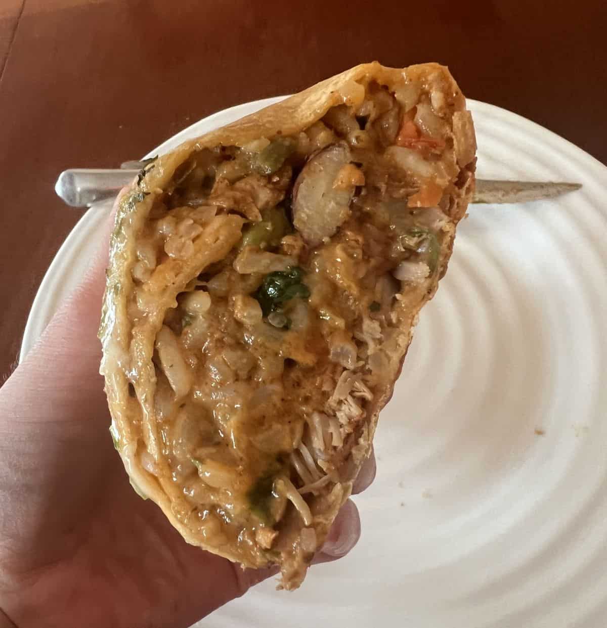 Closeup image of a hand holding one half pork Carnita cut in half and close to the camera so you can see the filling.