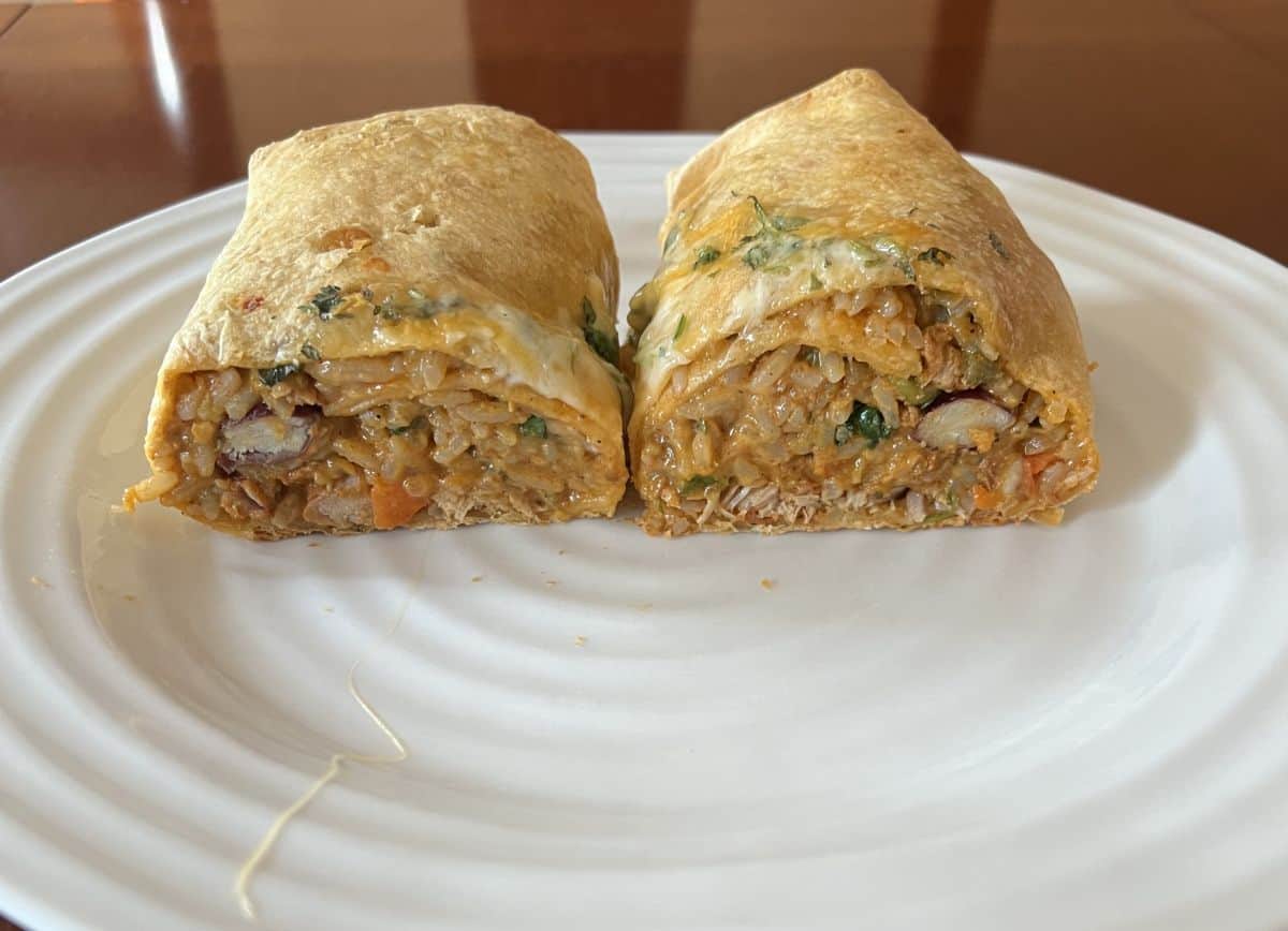 Image of one pork Carnita burrito served on a white plate and cut in half. 
