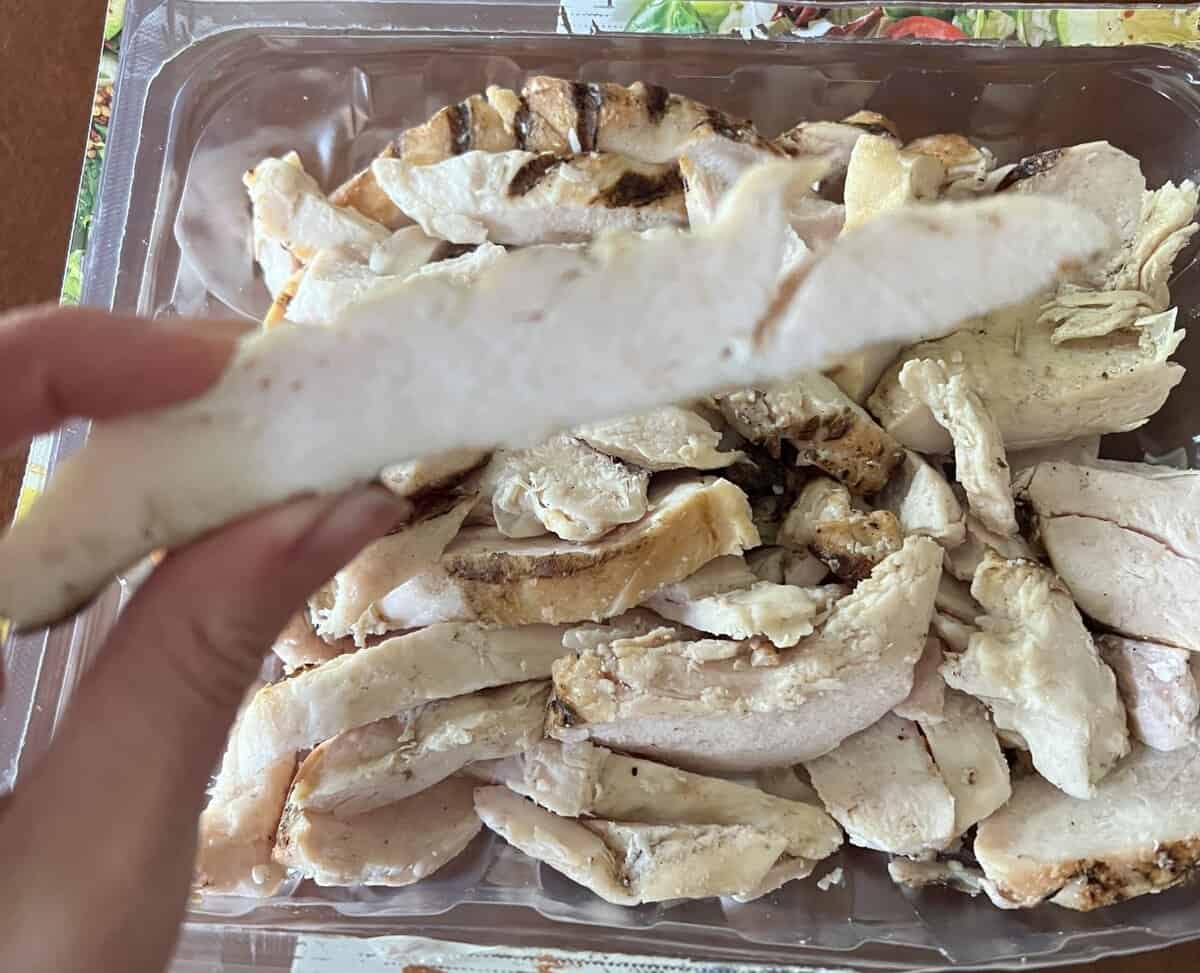 Image of a hand holding one chicken strip hovering over the package of chicken strips.