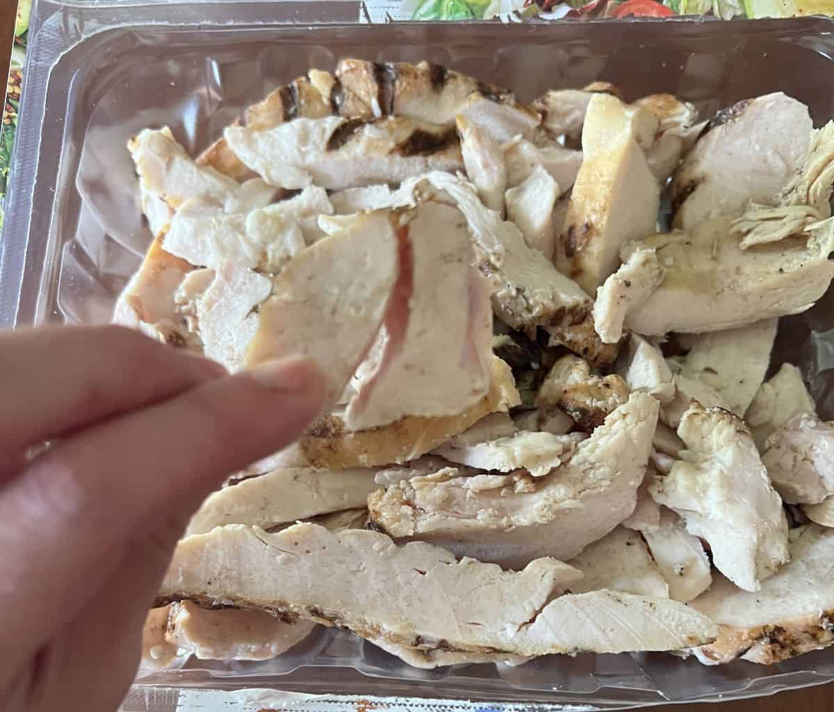 Image of a hand holding one chicken strip hovering over the package of chicken strips.