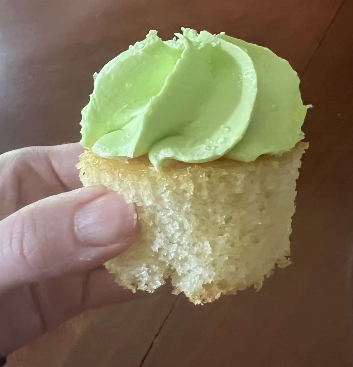 Image of a hand holding one lime cupcake close to the camera.