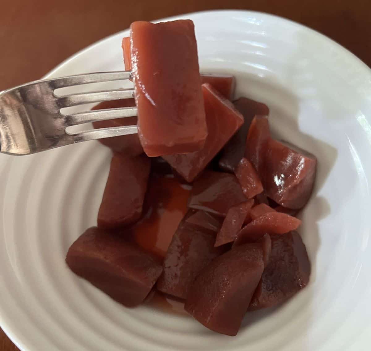 Image of a fork with a piece of beet on it hovering over a bowl of beet & onion salad.