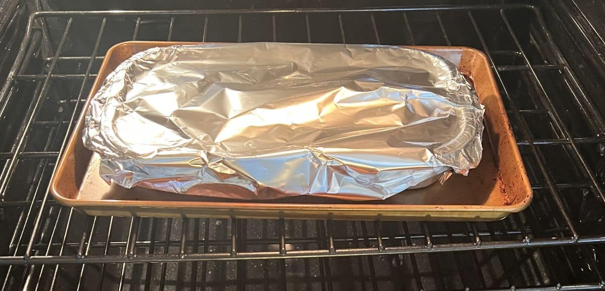 Image of a pierogi bake tray covered in aluminum foil on a cookie tray baking in the oven. 