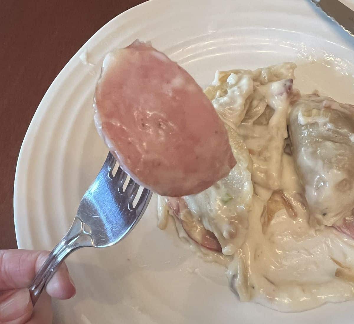 Image of a fork holding a slice of sausage hovering over a plate of the pierogi bake.