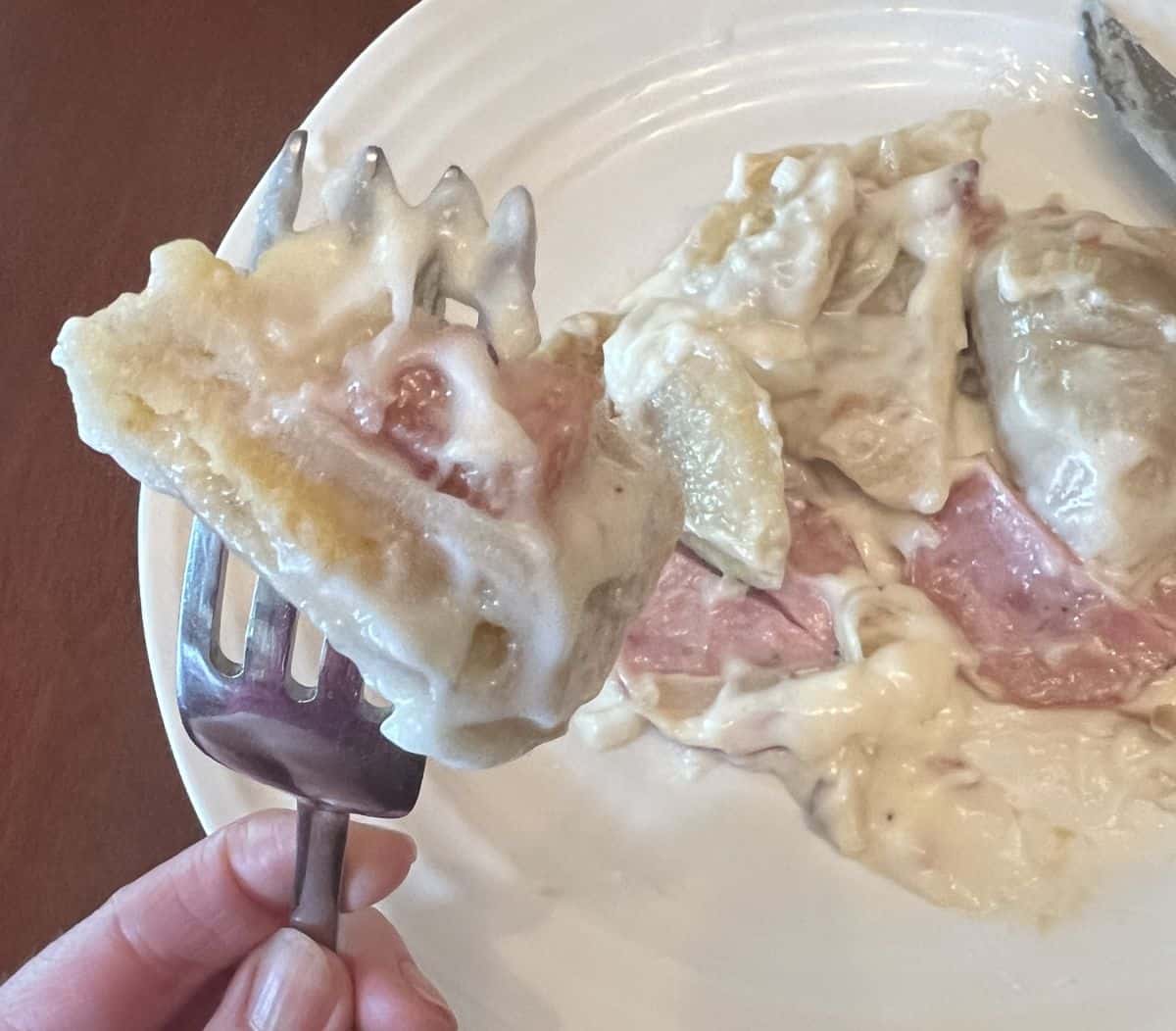 Image of a fork with pierogi and sausage on it hovering over a plate.