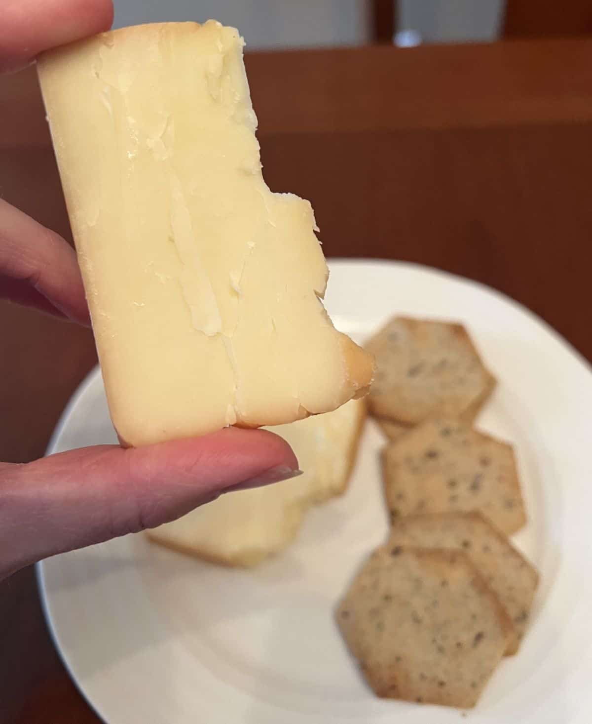 Image of a hand holding one slice of smoked cheddar hovering over a white plate with crackers on it.