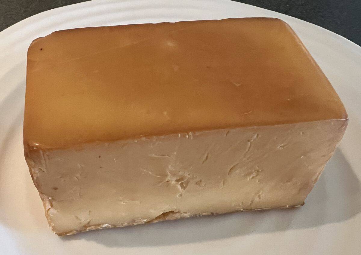 Top down image of an entire block of smoked double cheddar served on a white plate. 