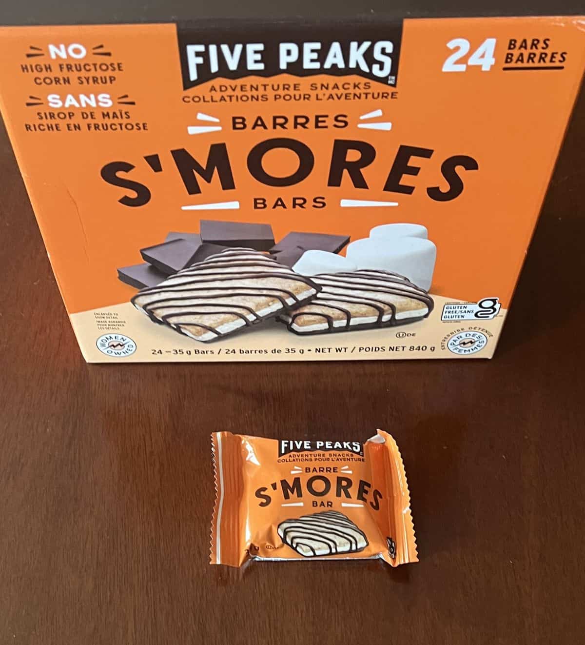 Image of one individually packaged s'mores bar sitting in front of the box of s'mores bars. 