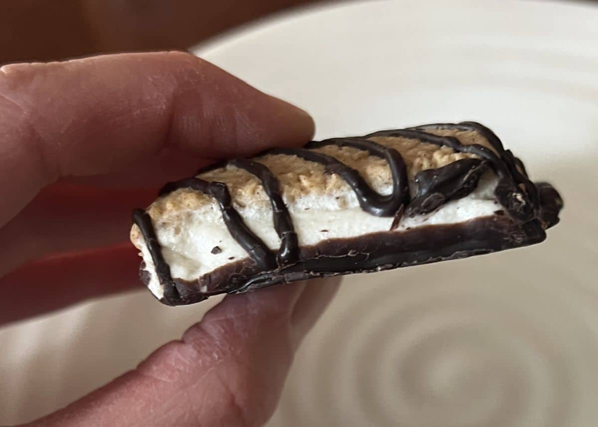 Closeup side view image of a hand holding one Costco Five Peaks S'mores Bar. 