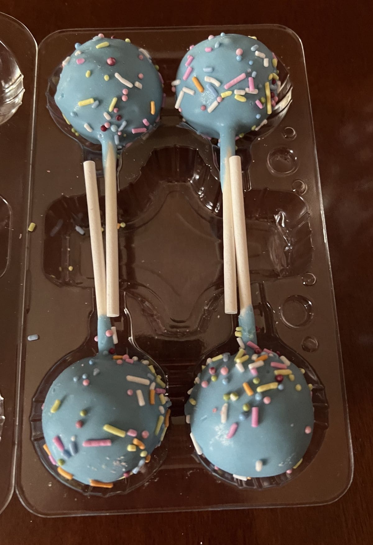 Image of four blue cake pops in a plastic container.