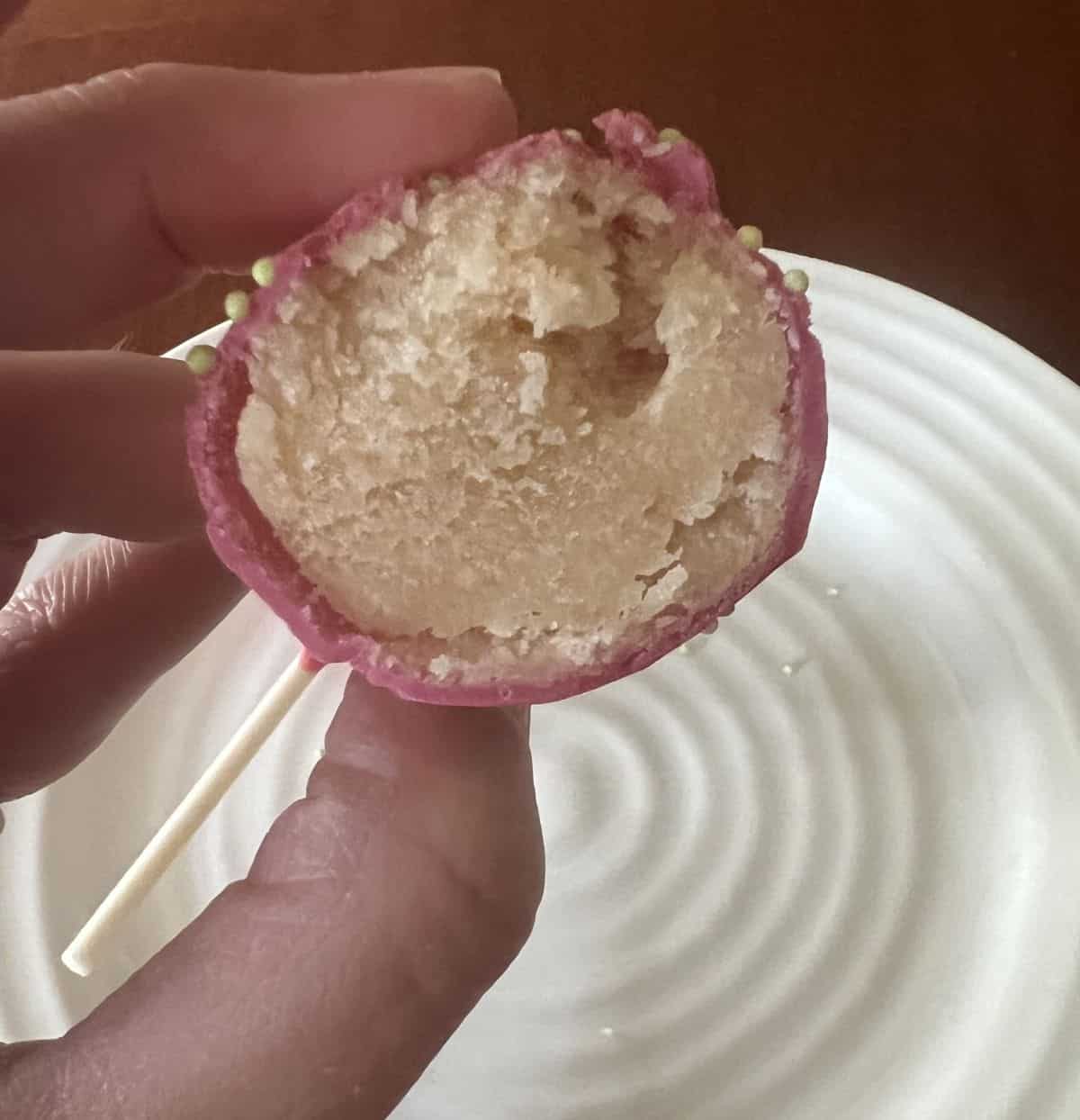 Image of a hand holding a piece of cake pop so you can see the cake inside and the icing. 