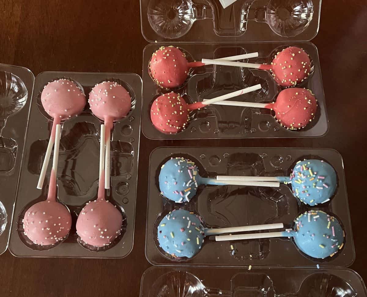 Image of 12 cake pops in three plastic containers. There are pink, blue and red ones.