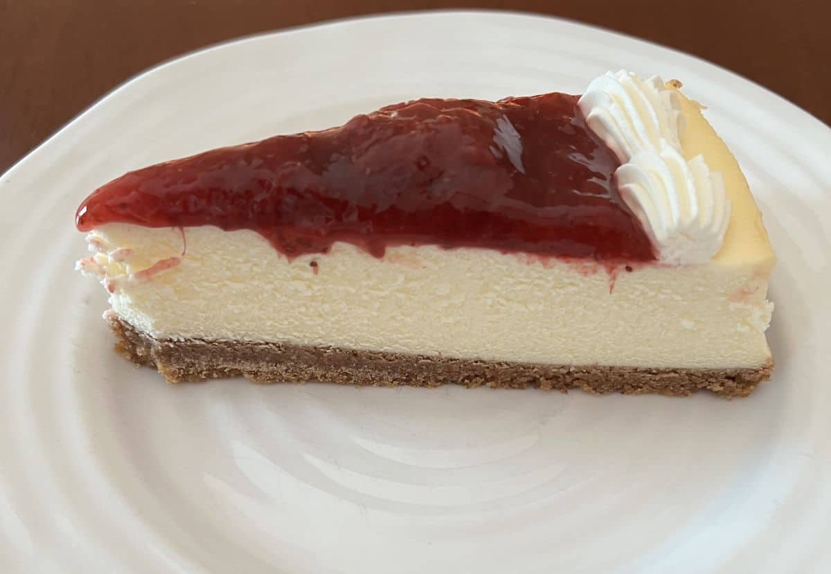 Sideview image of one slice of strawberry cheesecake served on a white plate. 