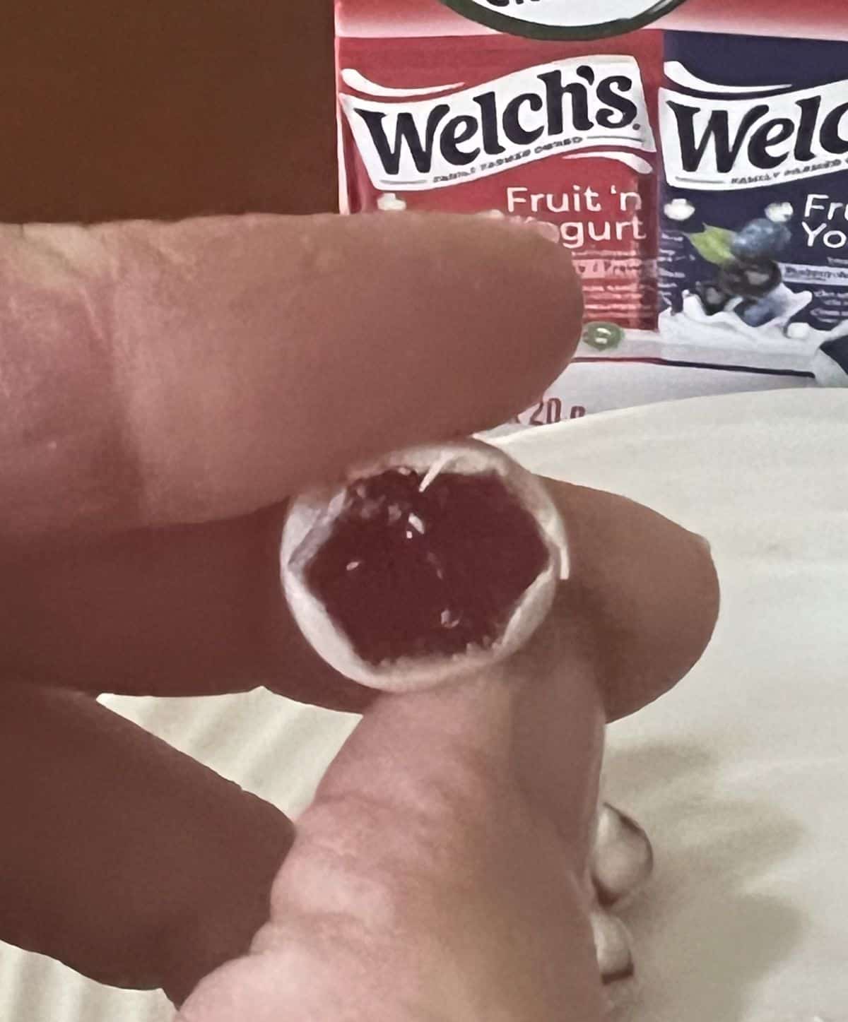 Image of a hand holding one strawberry fruit snack cut in half so you can see the center near the camera.