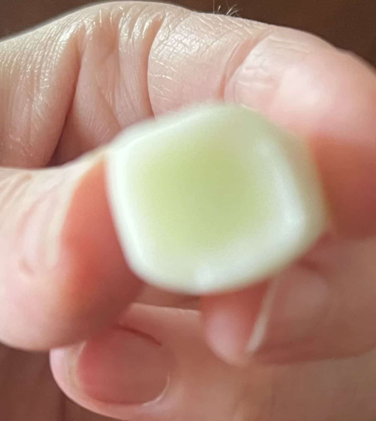 Closeup image of a hand holding one green apple Hi Chew close to the camera.