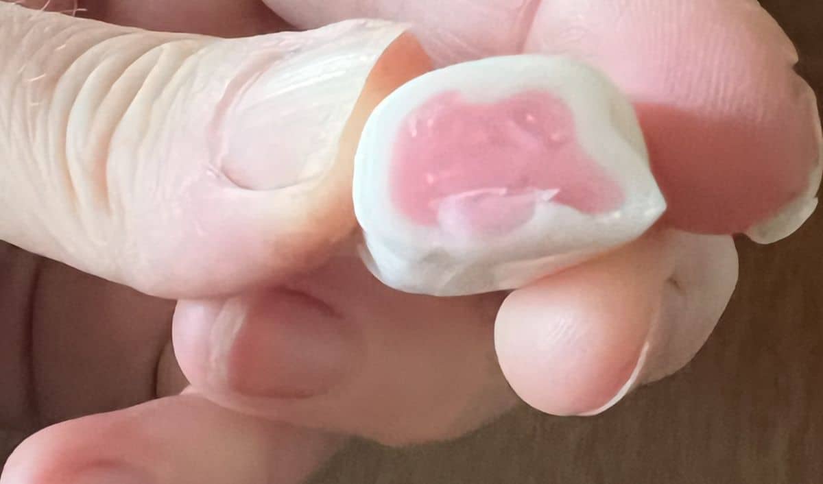 Image of a hand holding one strawberry Hi Chew close to the camera.
