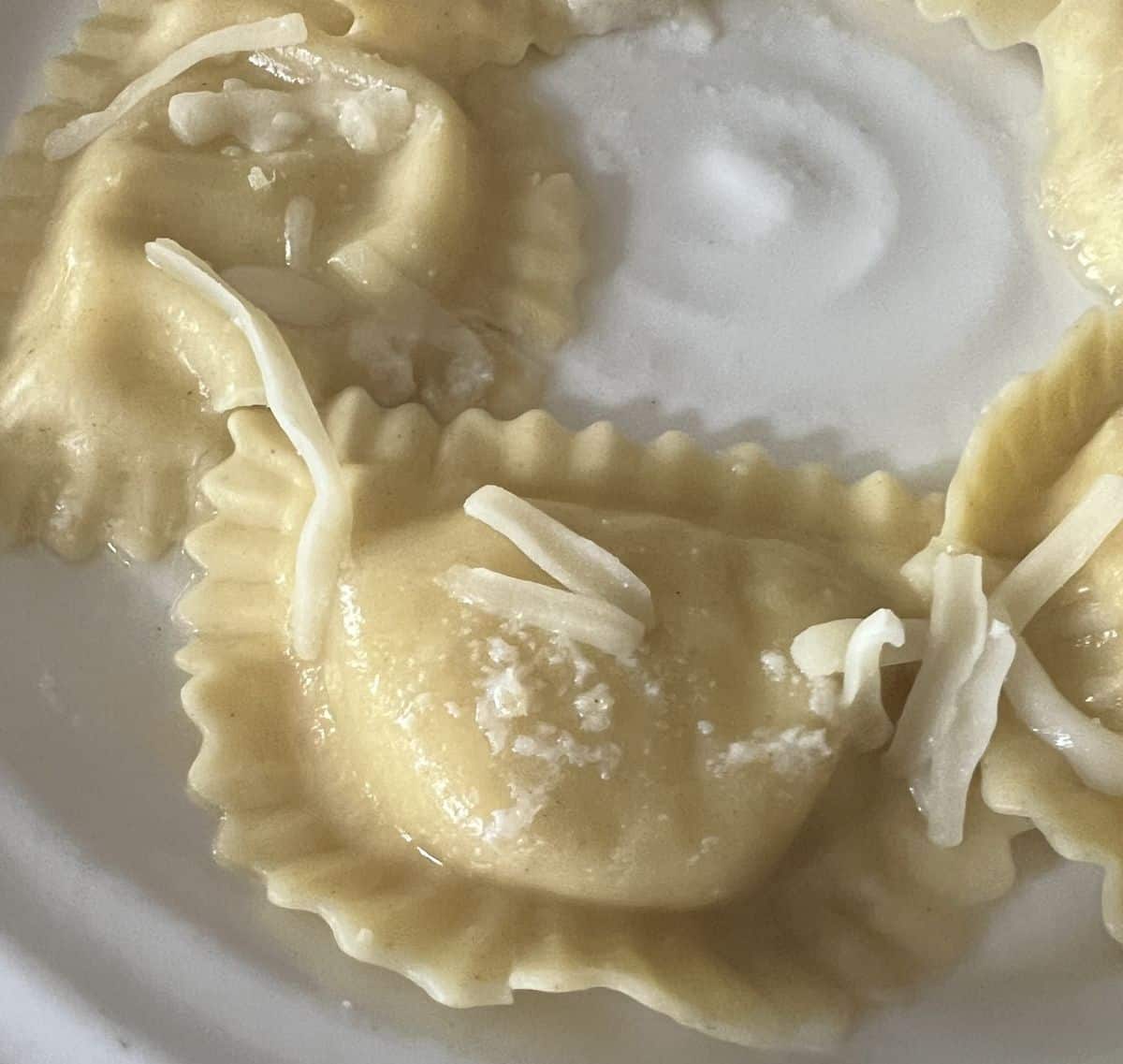Closeup image of a few ravioli served on a white plate with cheese sprinkled on top. 