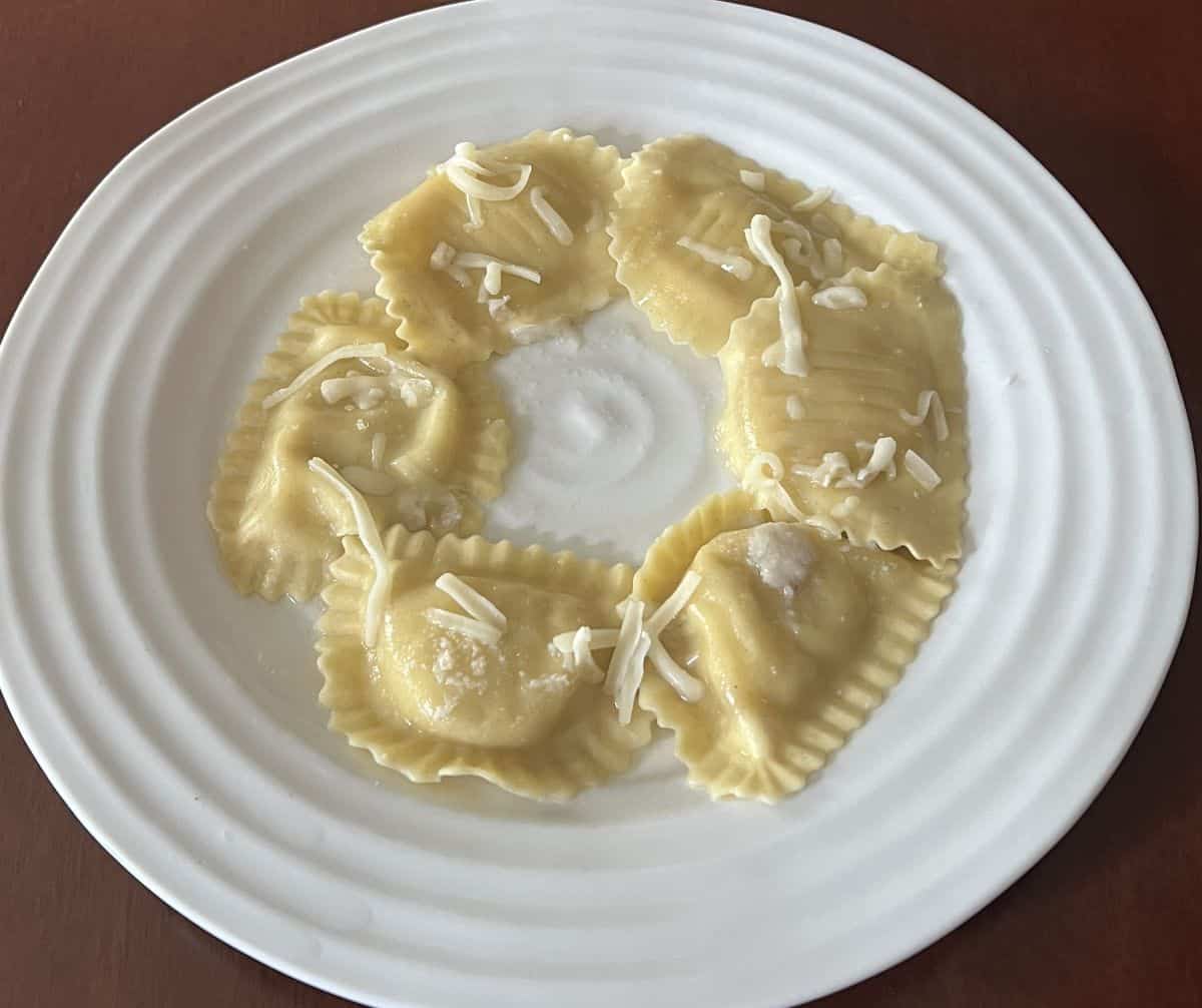 Image of a plate with six ravioli served on it, sprinkles with cheese and drizzled with olive oil. 