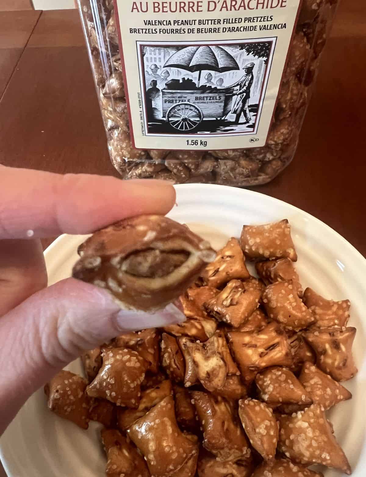 Image of a hand holding one peanut butter pretzel close to the camera so you can see the pretzel shell and peanut butter filling.
