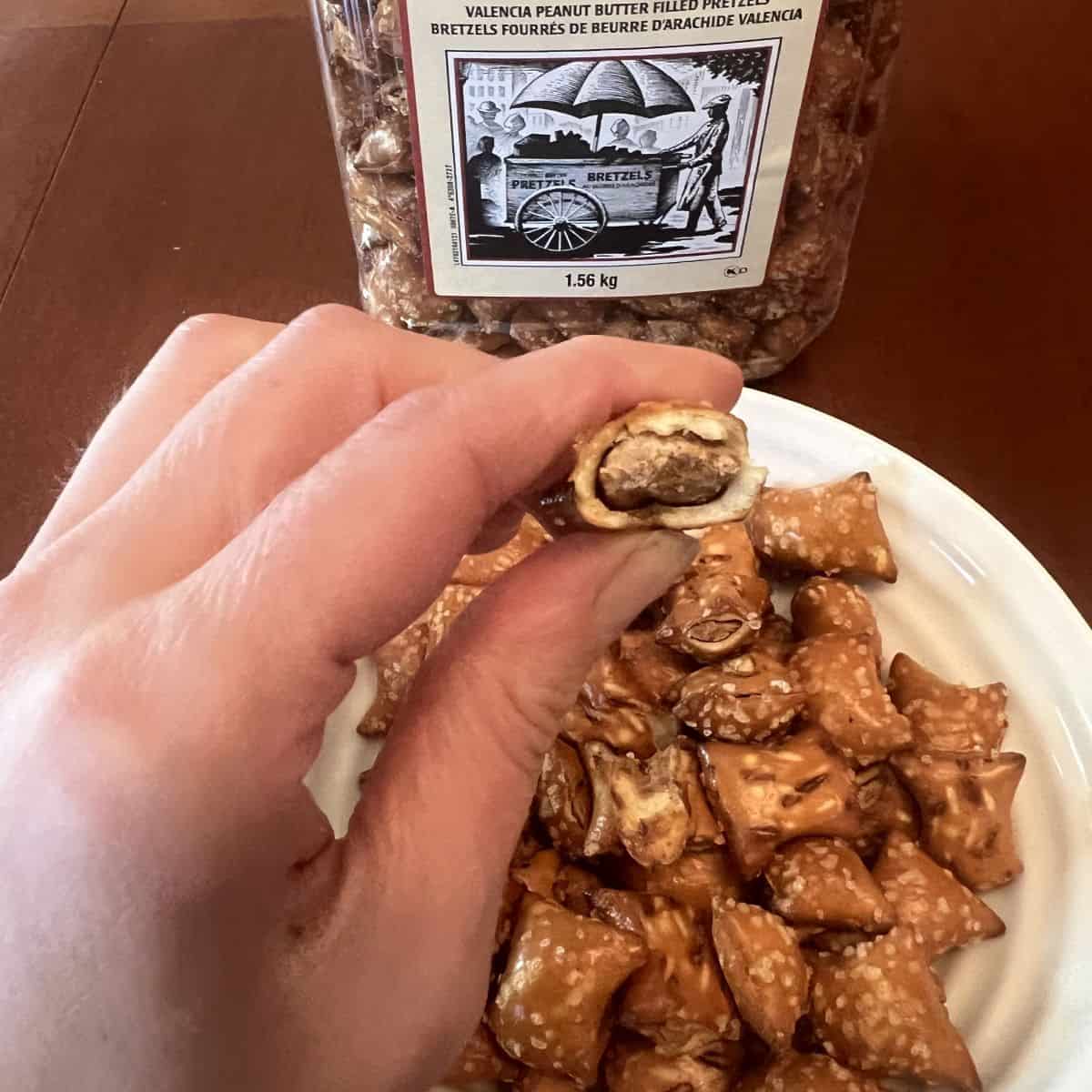Image of a hand holding one peanut butter pretzel with a bite taken out of it so you can see the center.
