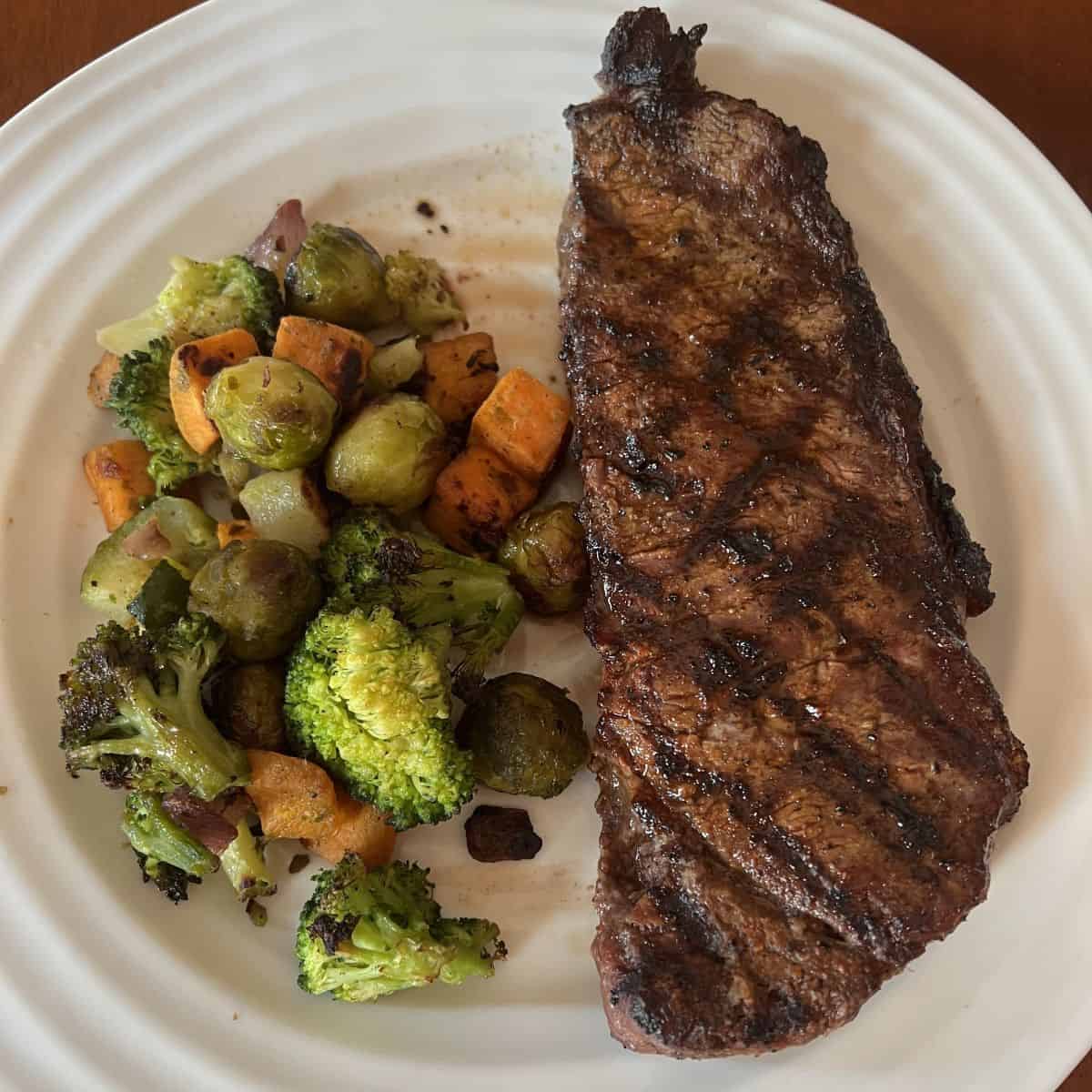 Image of a side of roasted vegetables beside a steak, served on a white plate.