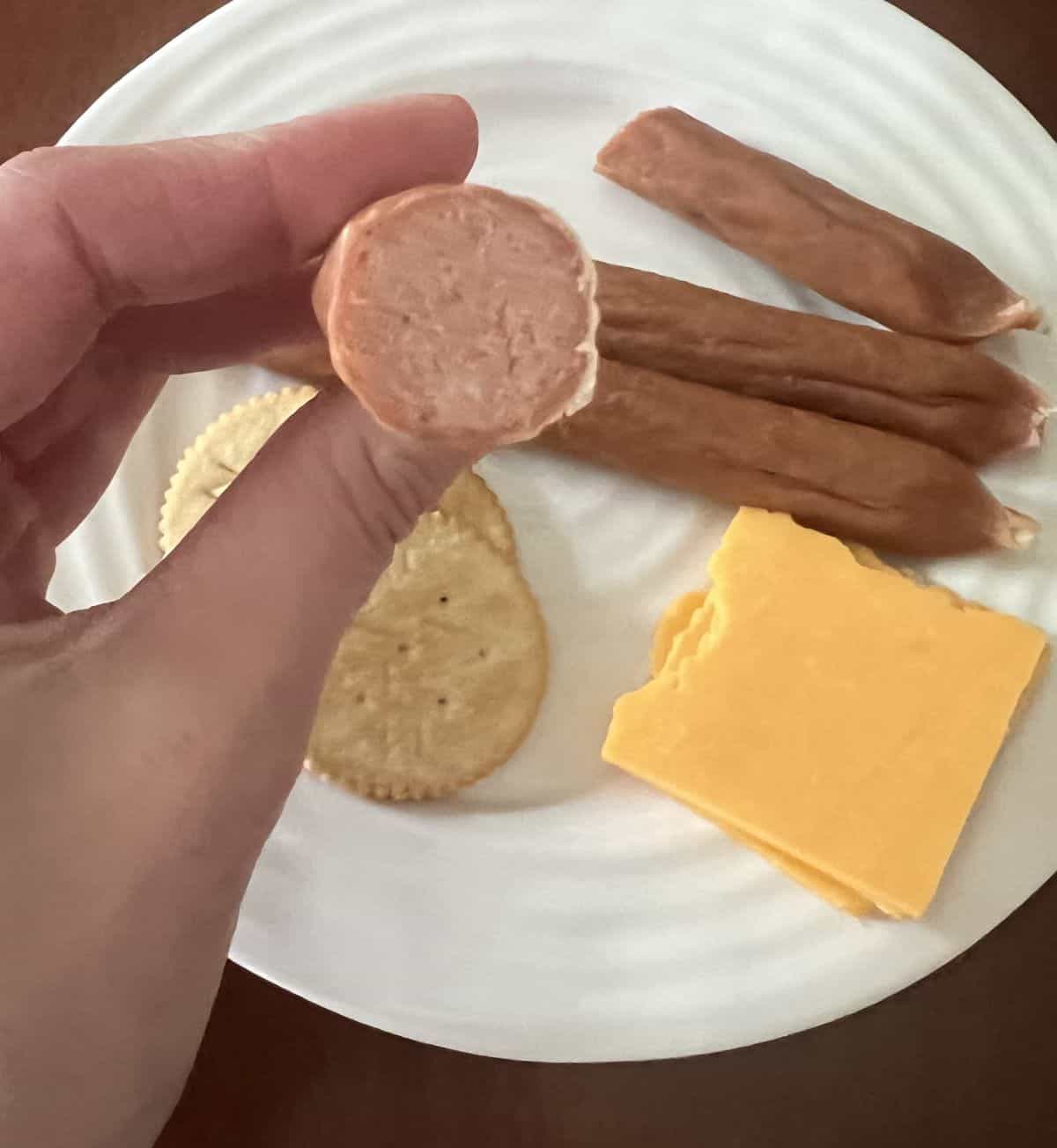 Image of a hand holding one turkey pepperoni cut in half so you can see what the inside looks like. 