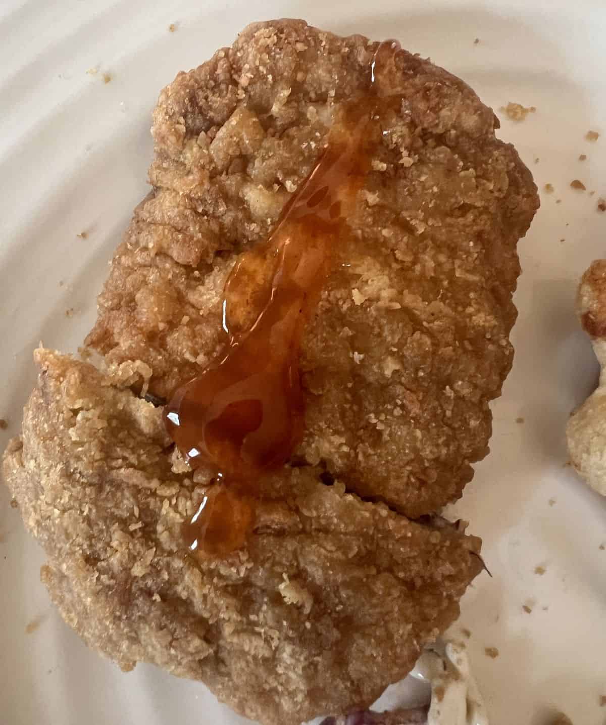 Top down image of a breaded chicken breast served on a white plate with hot honey drizzled on top. 