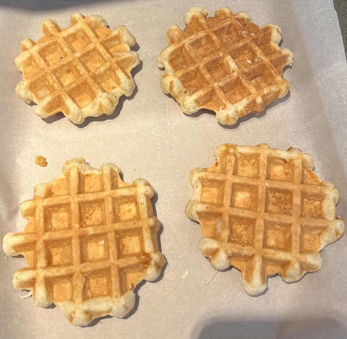 Image of four waffles on a parchment lined baking tray ready to be baked in the oven.