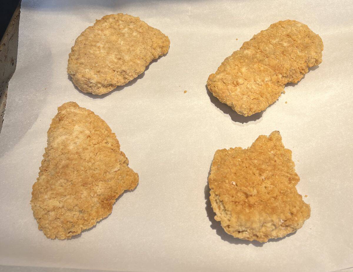 Image of four breaded chicken breasts on a parchment lined baking tray ready to be baked.