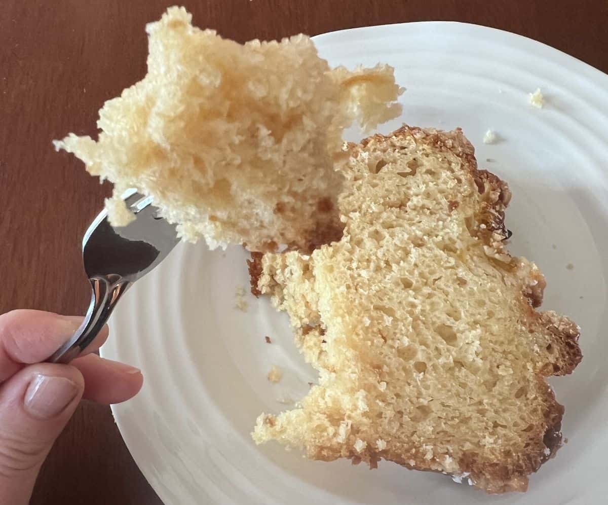 Closeup image of a fork with a bite of cake on it hovering over a plate of cake.