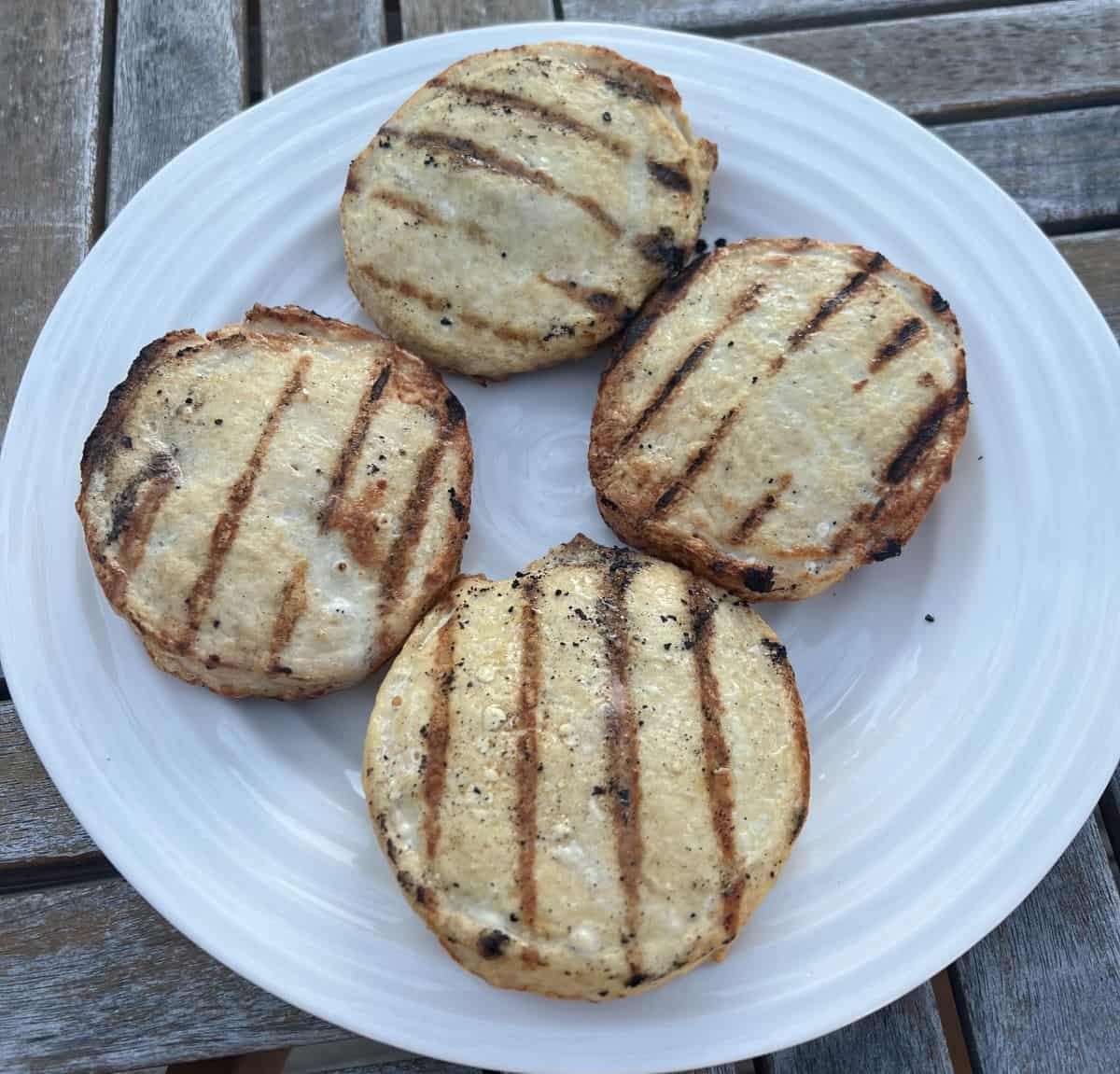 Top down image of four cooked chicken burgers served on a white plate.