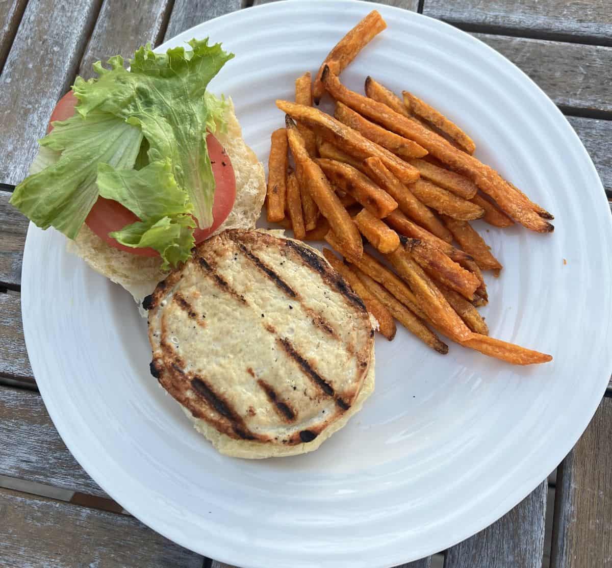 Image of one chicken breast burger in a bun with lettuce and tomato beside sweet potato fries.