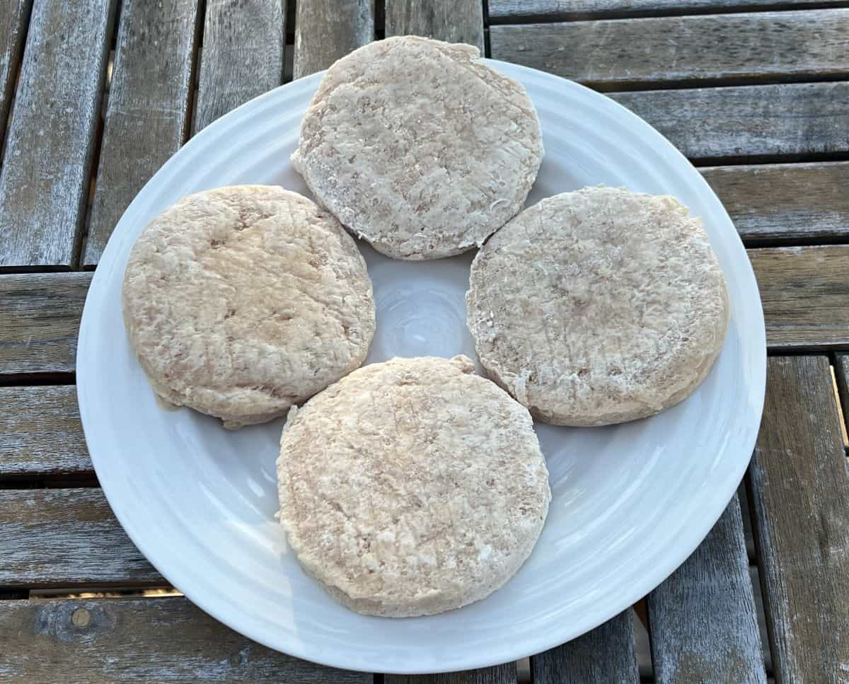 Image of four frozen chicken burger patties on a white plate prior to cooking them. 
