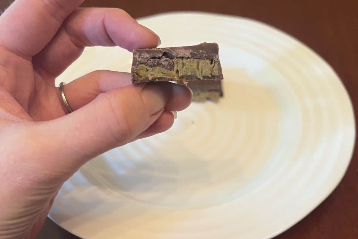 Closeup image of a hand holding one Dubai chocolate close to the camera cut in half so you can see the center.