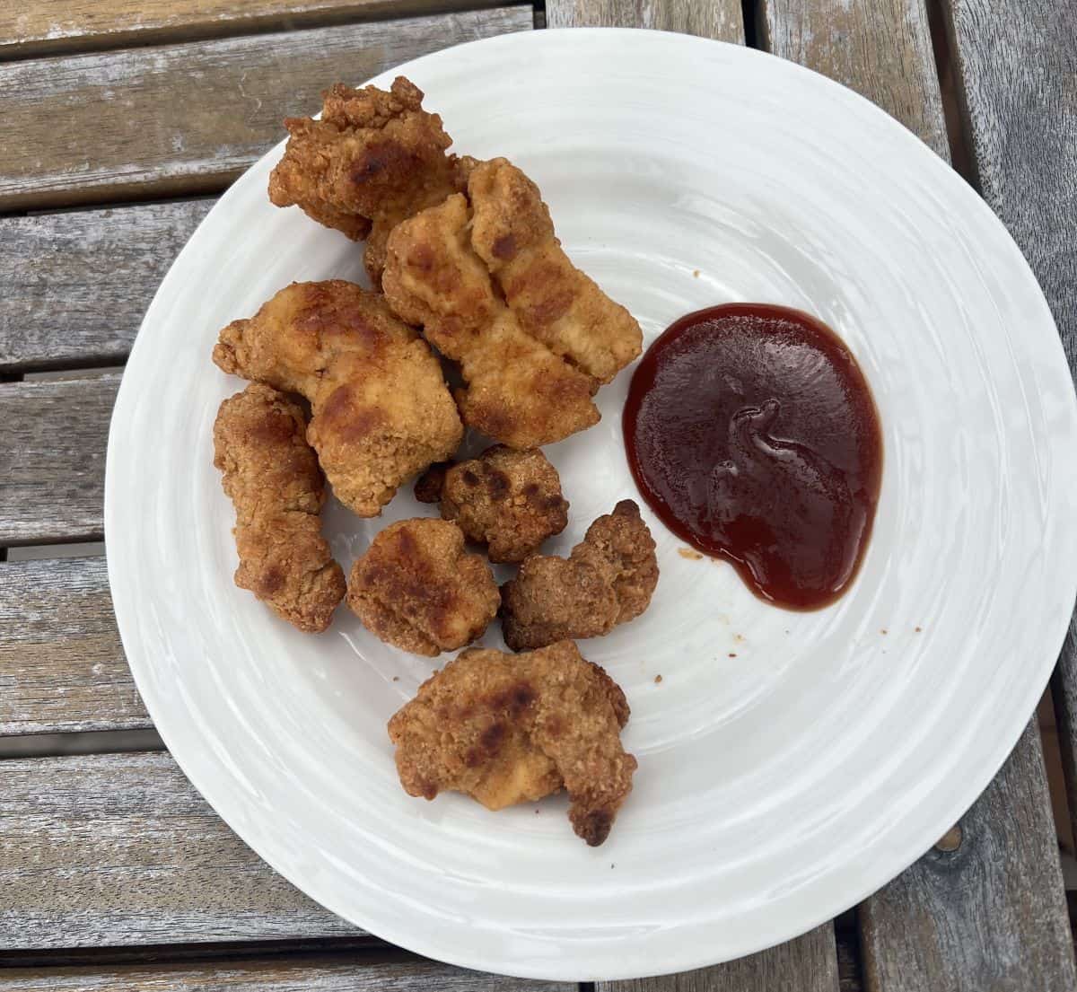 Image of the Kirkland Signature Lightly Breaded Chicken Breast chunks beside barbecue sauce on a white plate.