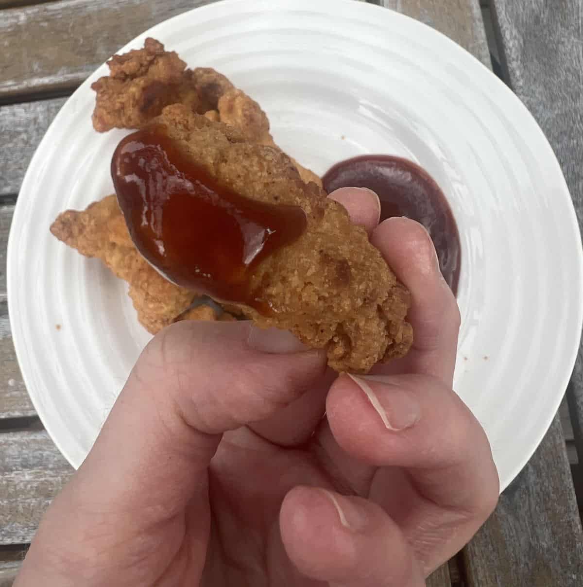Image of a hand holding one Kirkland Signature Chicken Breast Chunk with barbecue sauce on it. 