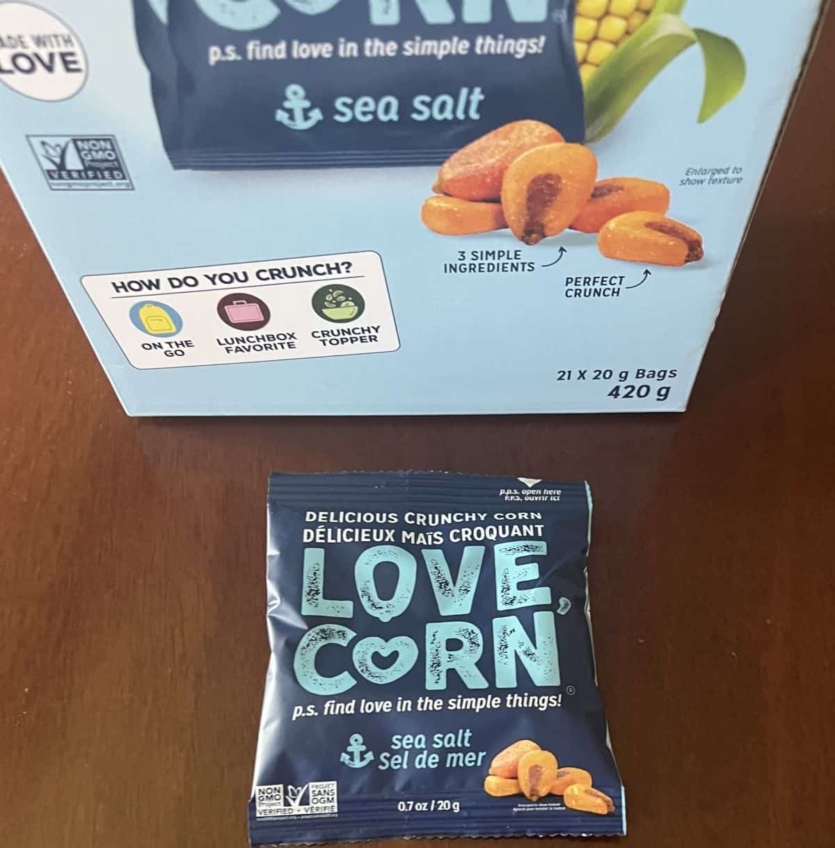 Image of one Love Corn snack pack unopened sitting in front of the box of Love Corn. 
