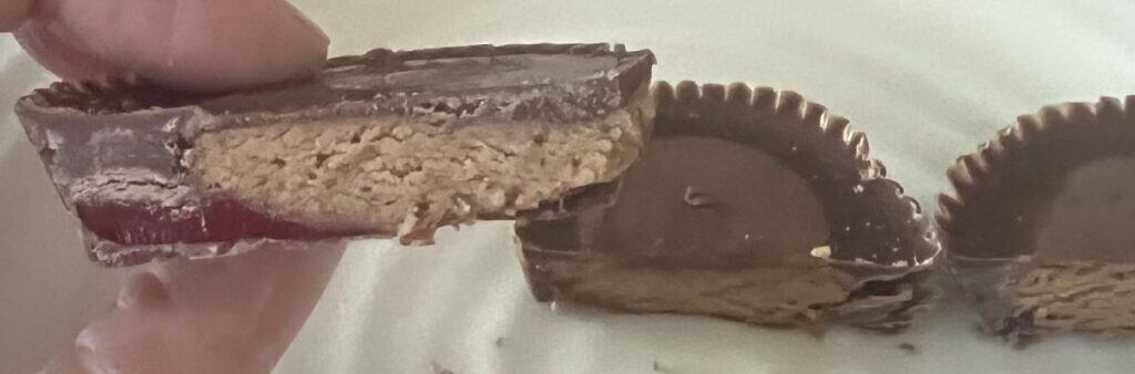 Closeup image of a hand holding one Reese's Peanut Buter Cup cut in half with strawberry filling on the inside. 